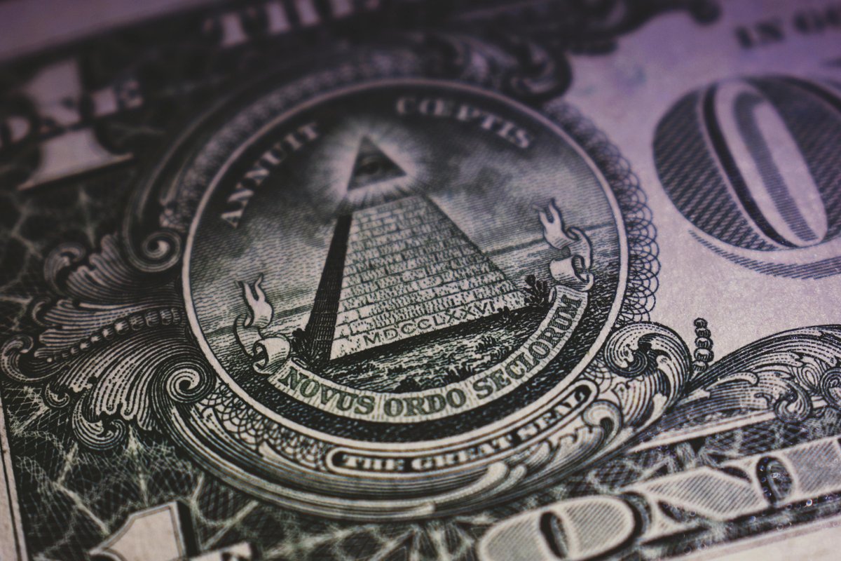 A close-up of the Great Seal on the back of a U.S. one-dollar bill, showing the pyramid with an eye at the top and the words 'Annuit Coeptis' and 'Novus Ordo Seclorum' in Latin, with detailed engraving patterns around the seal.