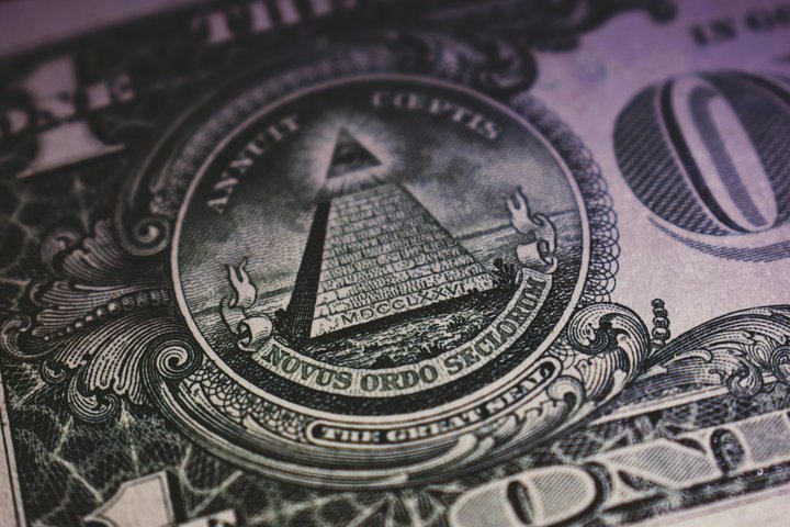A close-up of the Great Seal on the back of a U.S. one-dollar bill, showing the pyramid with an eye at the top and the words 'Annuit Coeptis' and 'Novus Ordo Seclorum' in Latin, with detailed engraving patterns around the seal.